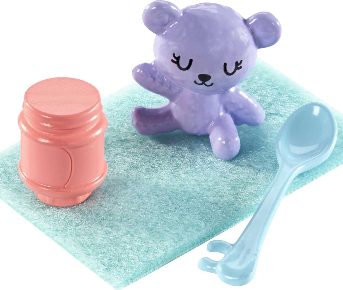 Purple teddy bear, pink jar, and blue spoon on a green mat